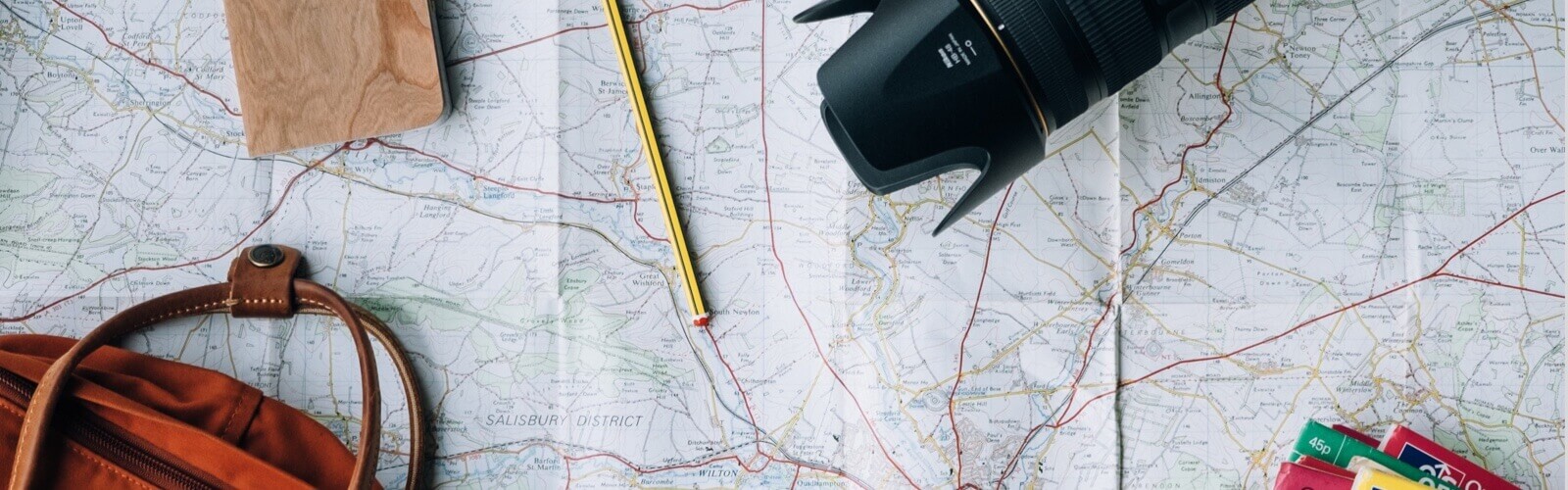 A camera, pencil, and bag laying ontop of a world map