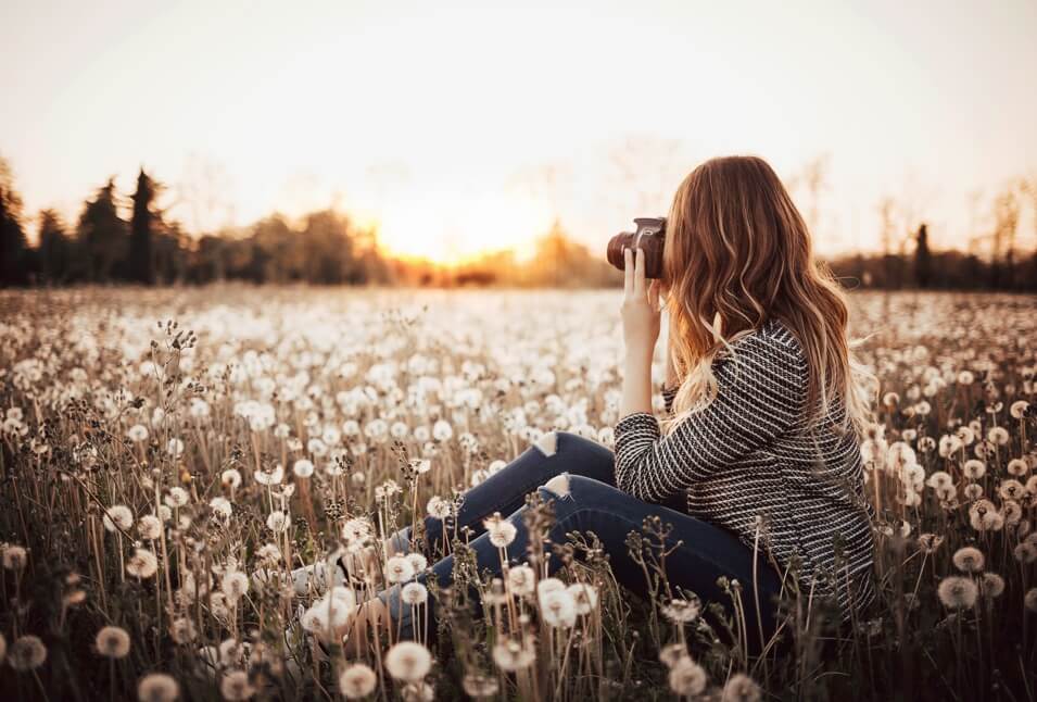 A woman holding a camera sitting in a field